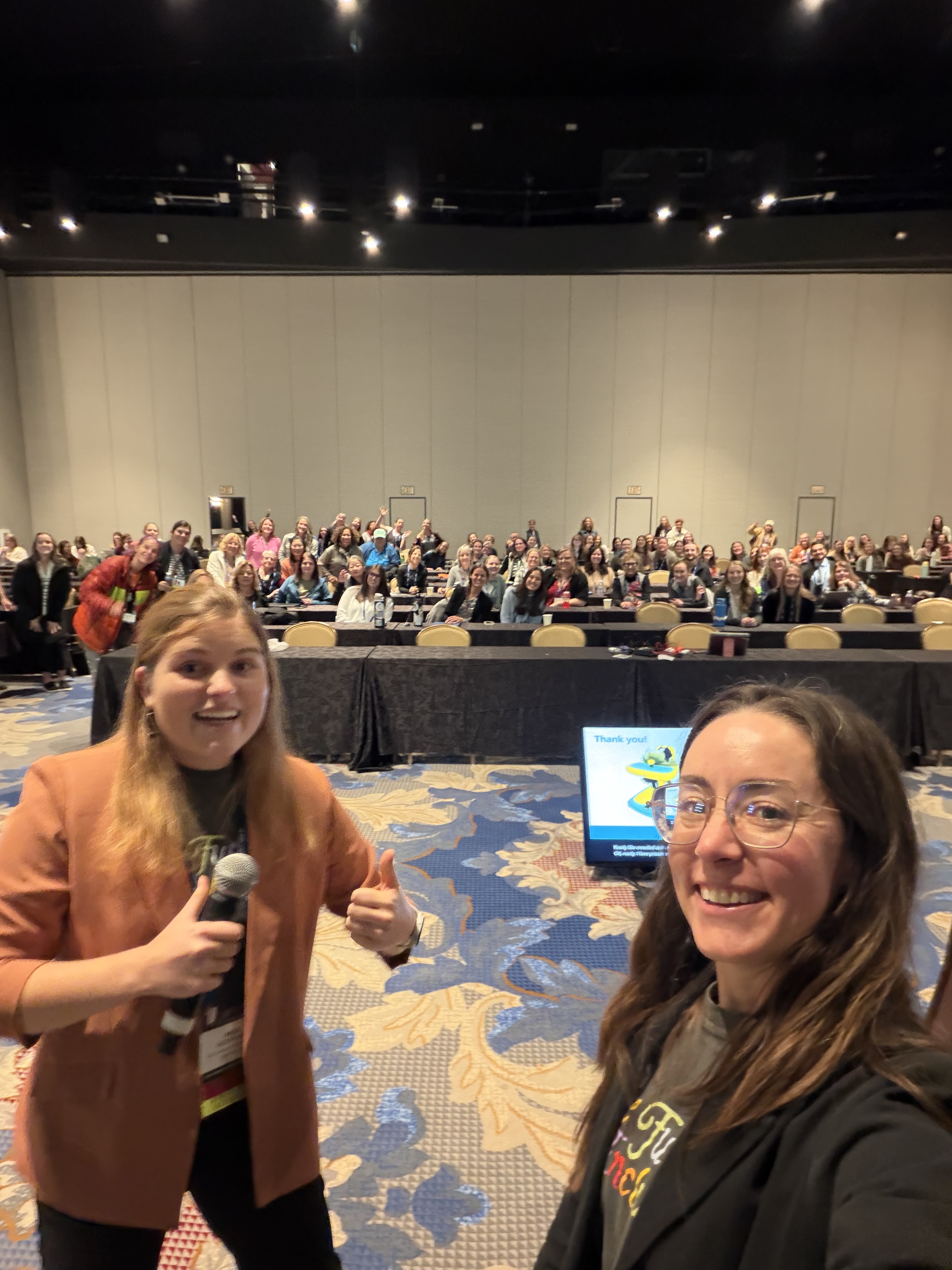 Mia and Bethany Sloane taking a selfie with a crowd of over 100 at a conference education session.