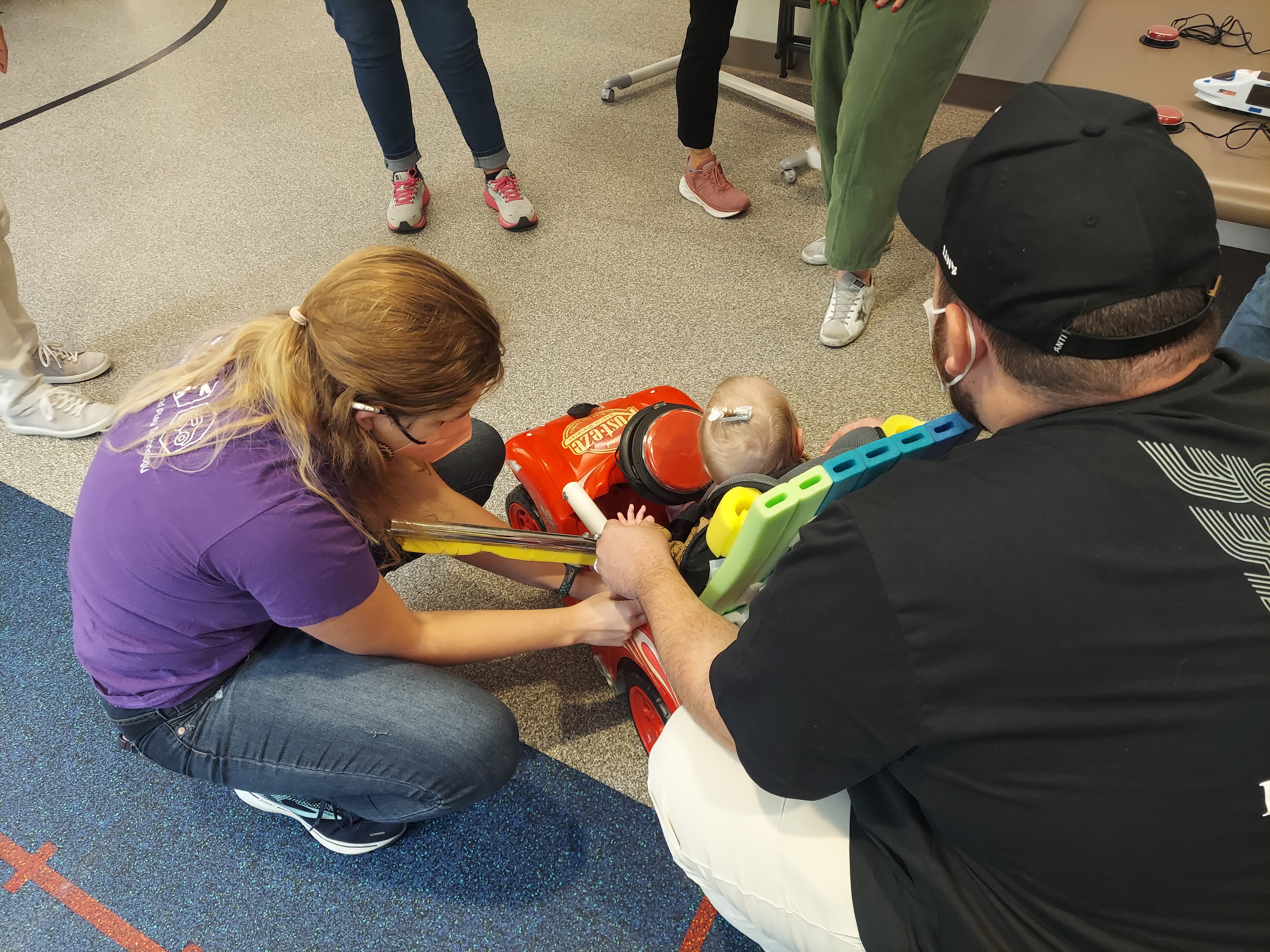 Mia fitting a young child to a GoBabyGo adapted ride-on car