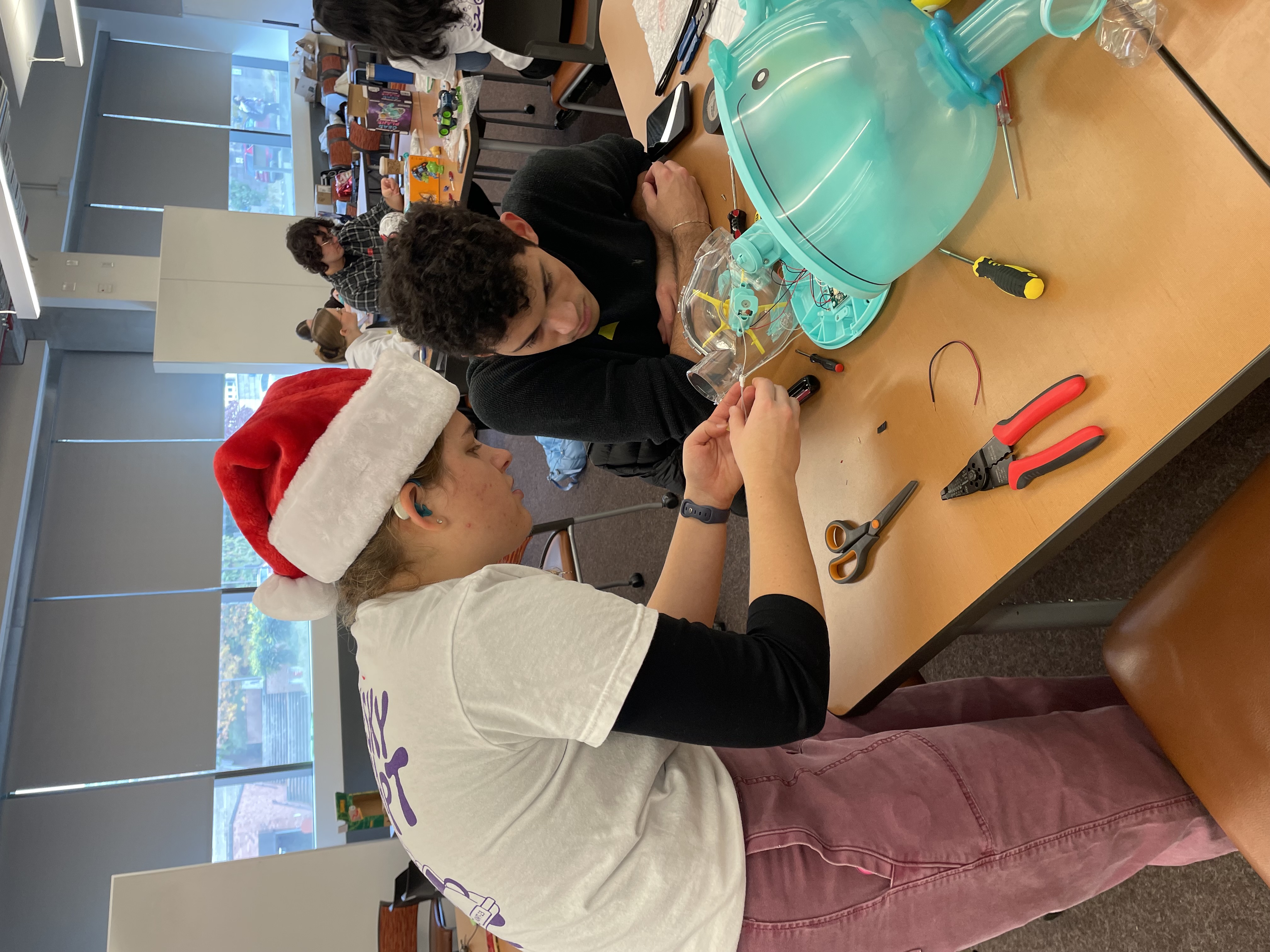 Mia wearing a Santa hat helping someone troubleshoot the adaptation of a toy bubble blower.