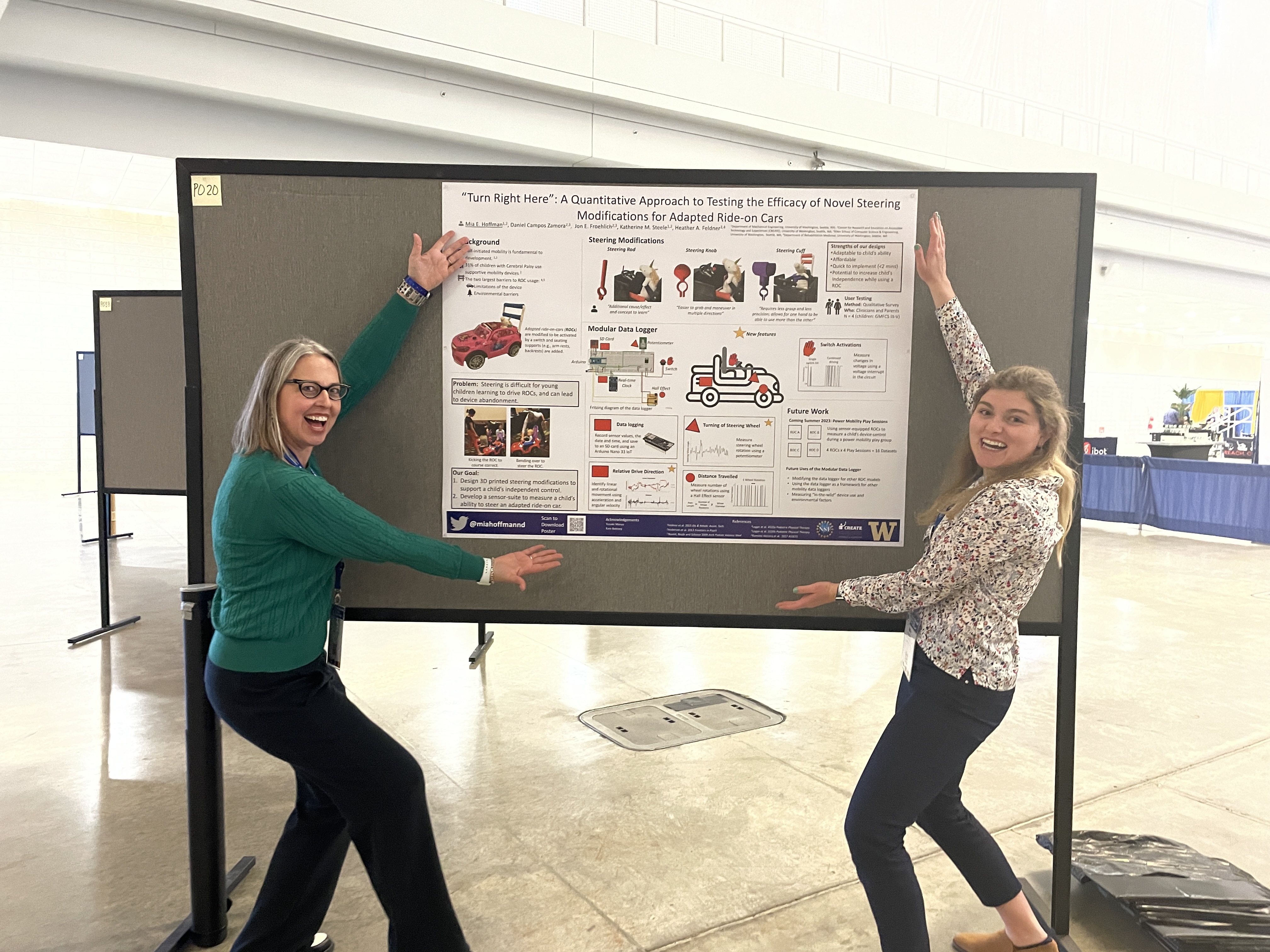 Mia and Heather dramatically showing off a poster with an adapted ride-on car on it.